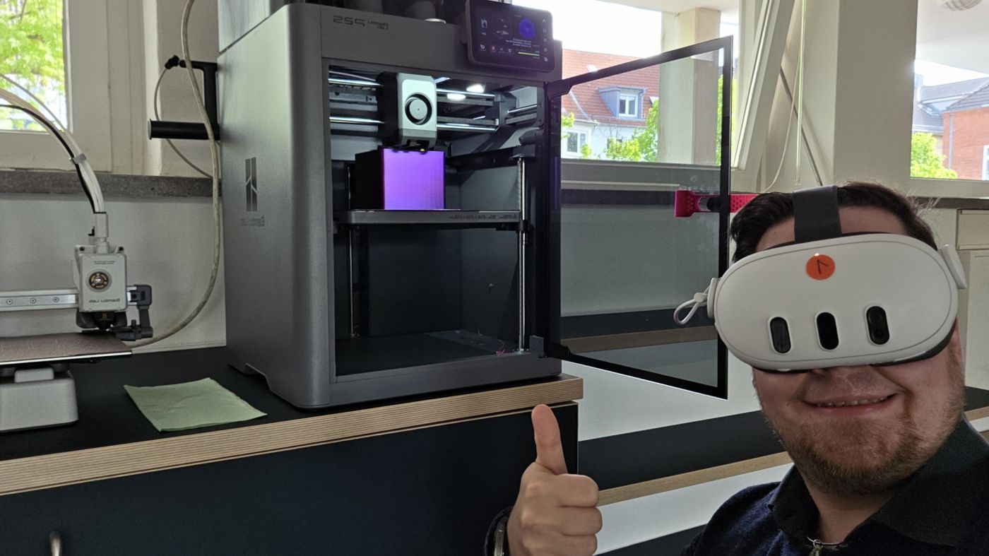 Christian Vogel mit VR-Brille und Daumen hoch vor einem 3D-Drucker